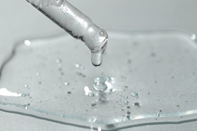 Photo of Dripping cosmetic serum from pipette on light background, closeup