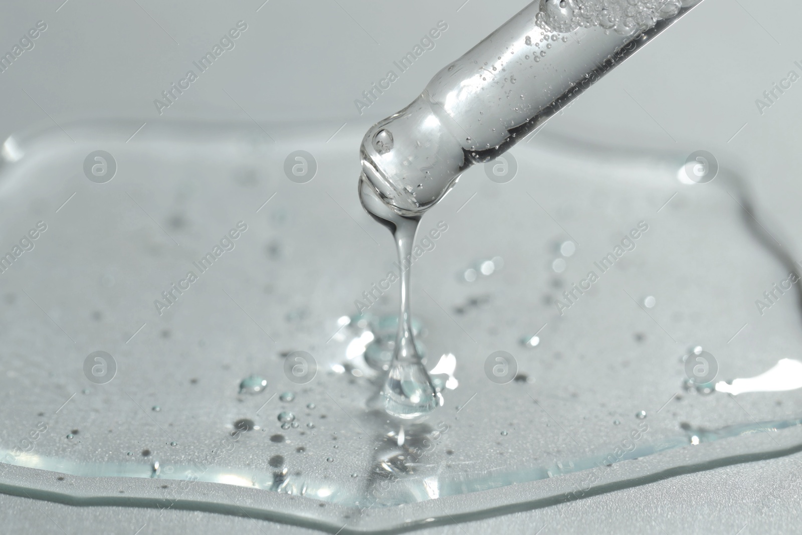 Photo of Dripping cosmetic serum from pipette on light background, closeup