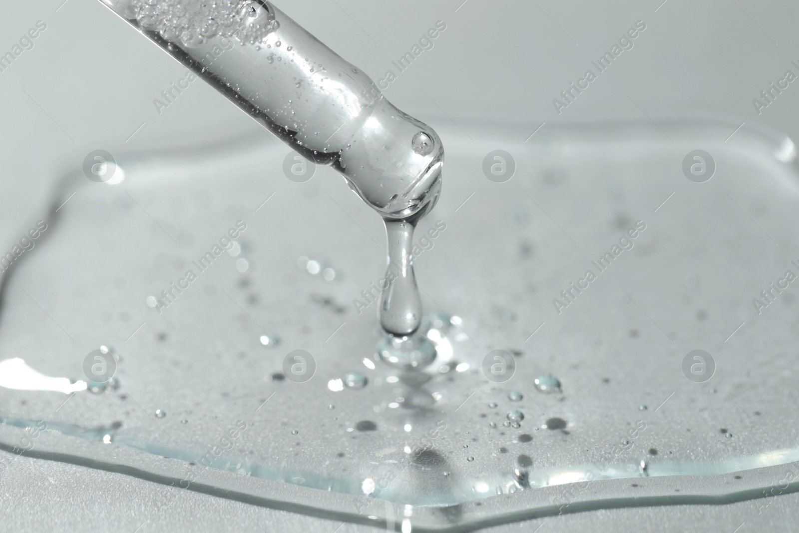 Photo of Dripping cosmetic serum from pipette on light background, closeup