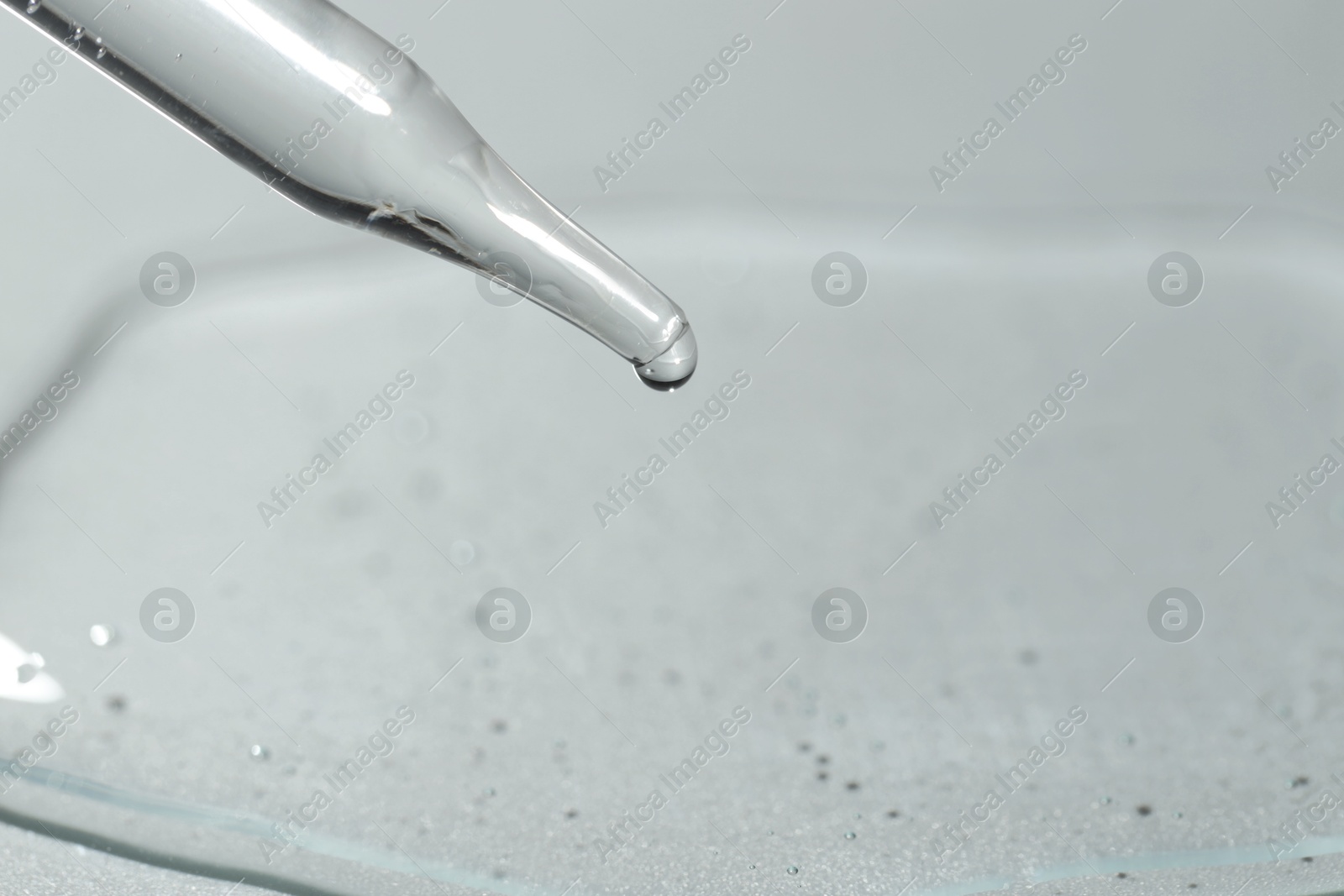 Photo of Dripping cosmetic serum from pipette on light background, closeup