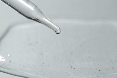 Dripping cosmetic serum from pipette on light background, closeup