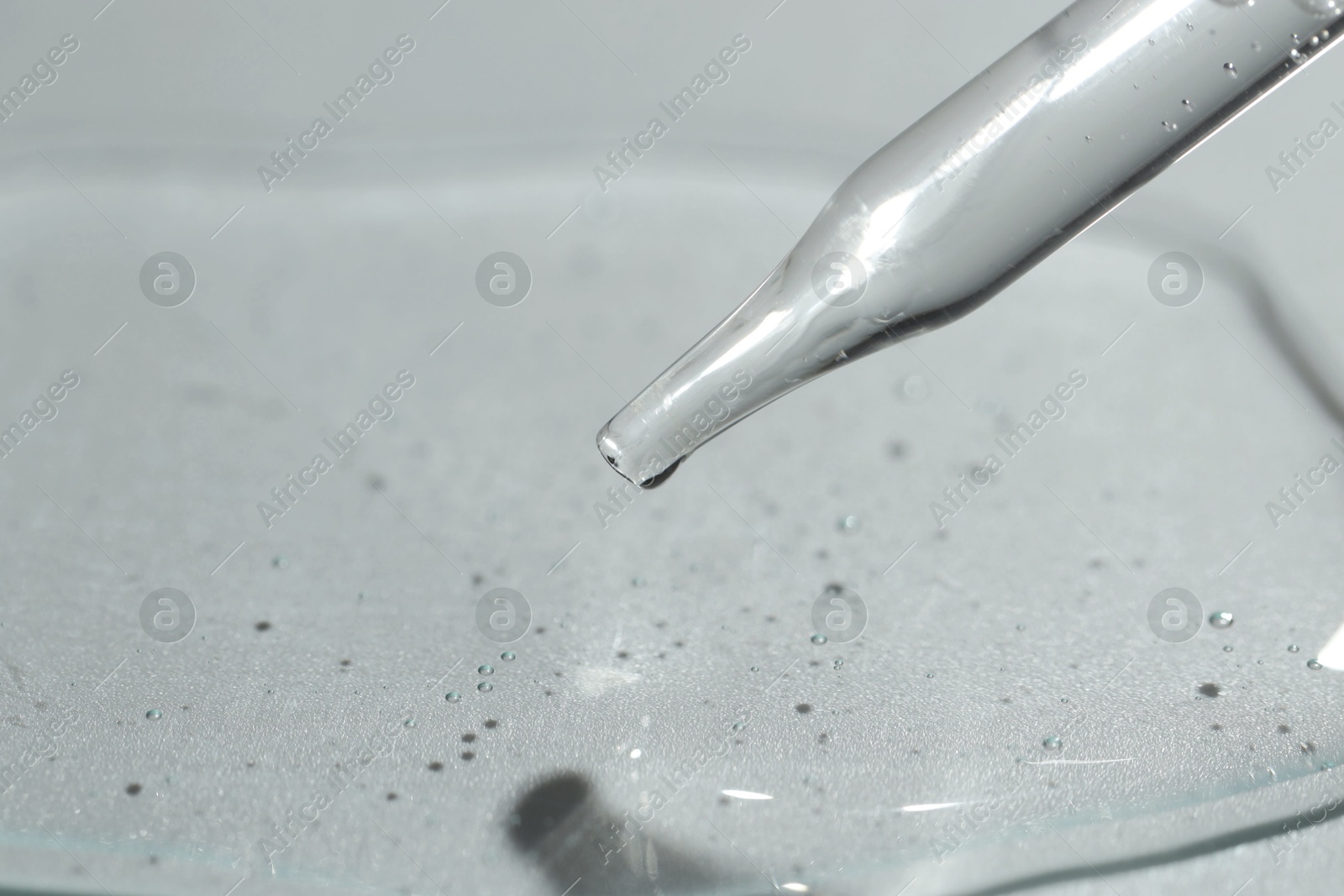 Photo of Dripping cosmetic serum from pipette on light background, closeup