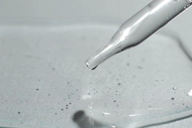 Dripping cosmetic serum from pipette on light background, closeup