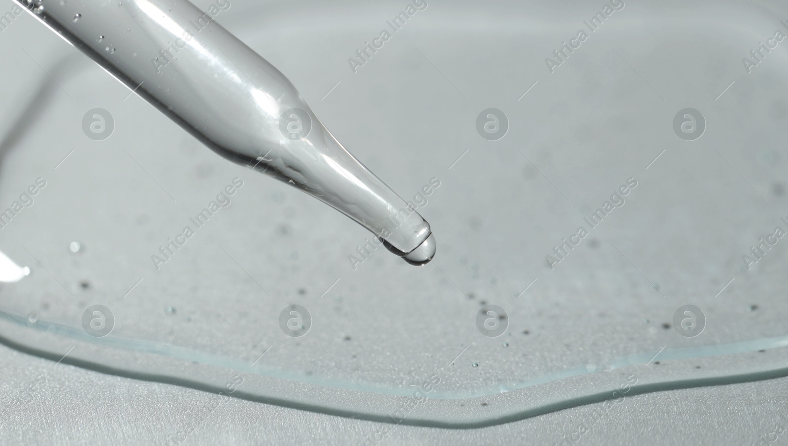 Photo of Dripping cosmetic serum from pipette on light background, closeup