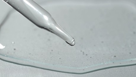 Dripping cosmetic serum from pipette on light background, closeup