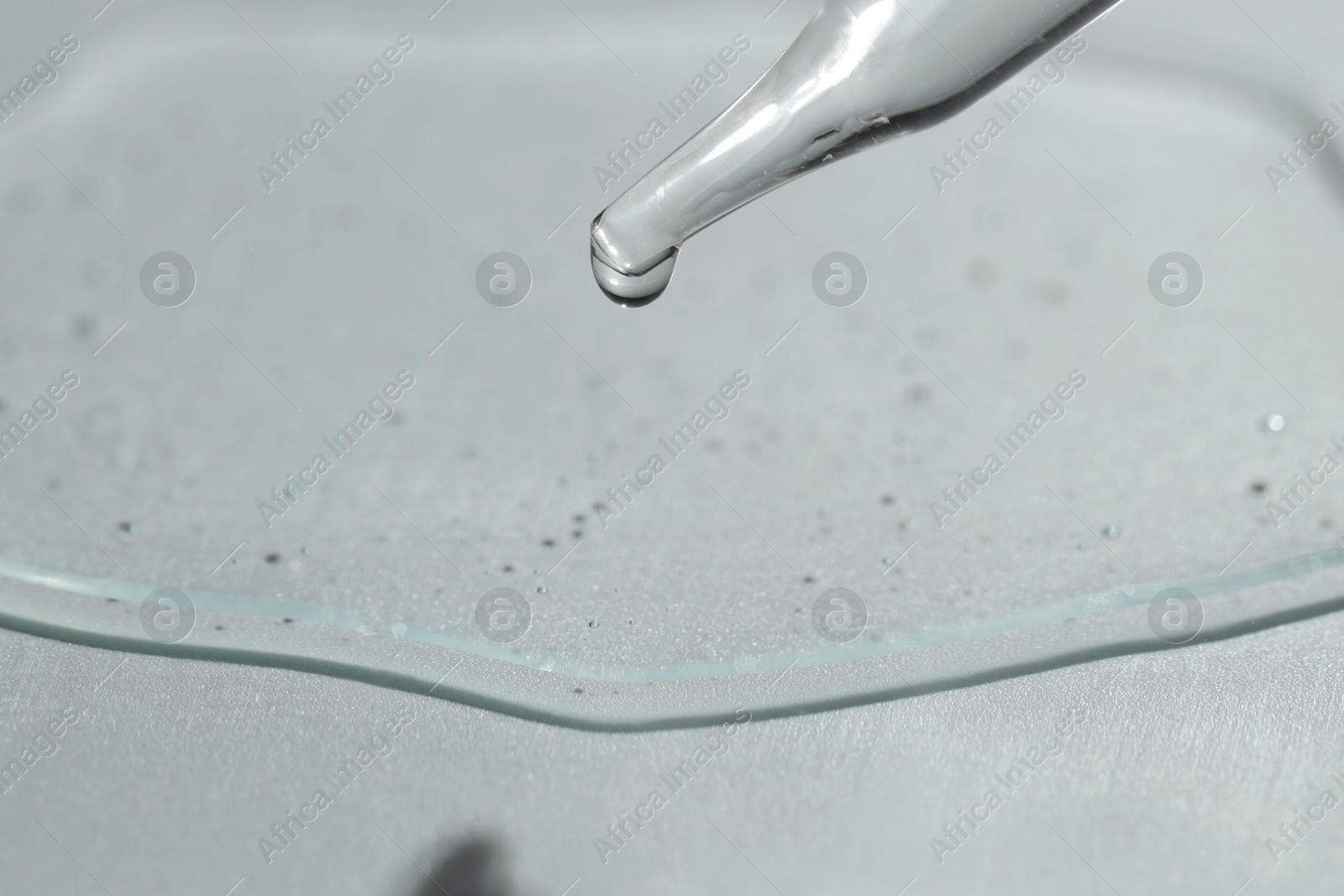 Photo of Dripping cosmetic serum from pipette on light background, closeup