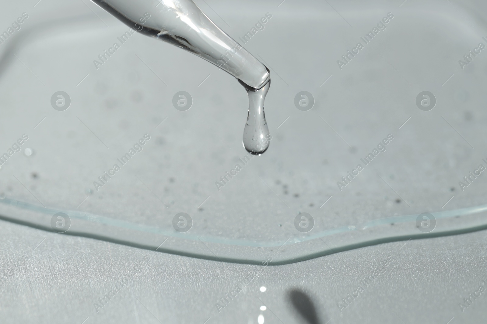 Photo of Dripping cosmetic serum from pipette on light background, closeup