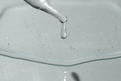 Photo of Dripping cosmetic serum from pipette on light background, closeup