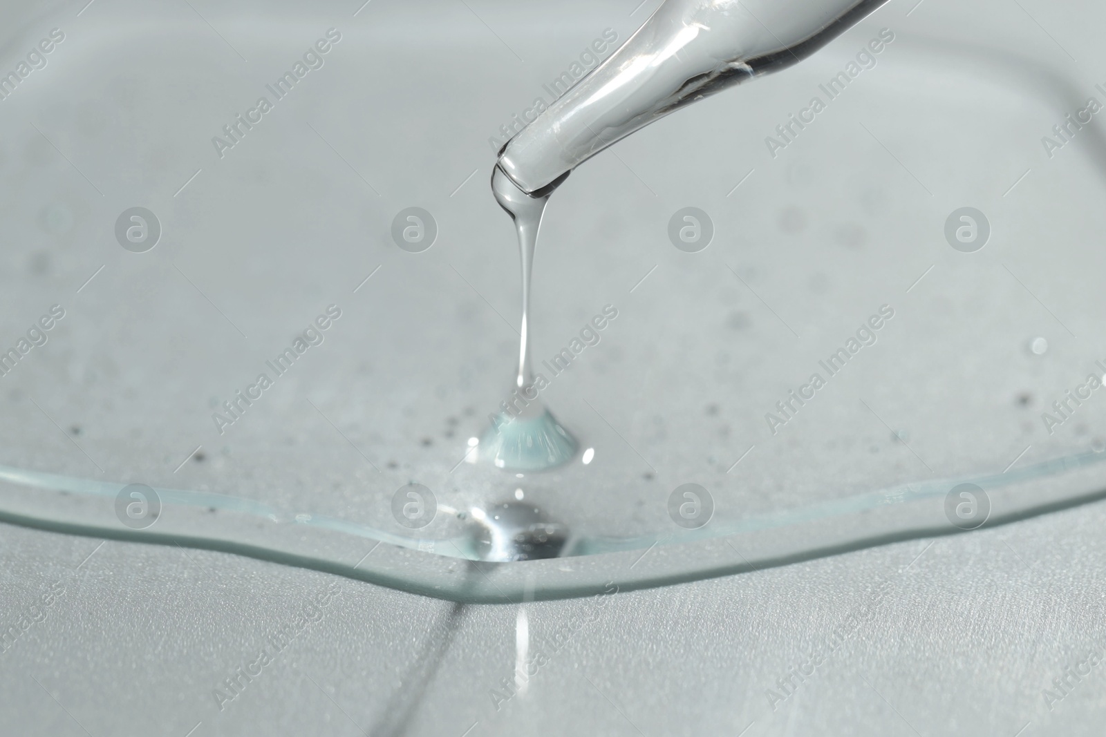 Photo of Dripping cosmetic serum from pipette on light background, closeup