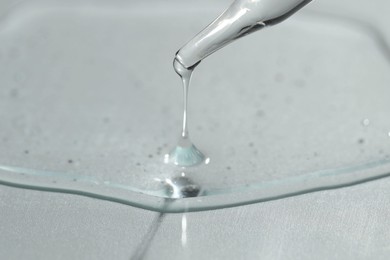 Photo of Dripping cosmetic serum from pipette on light background, closeup