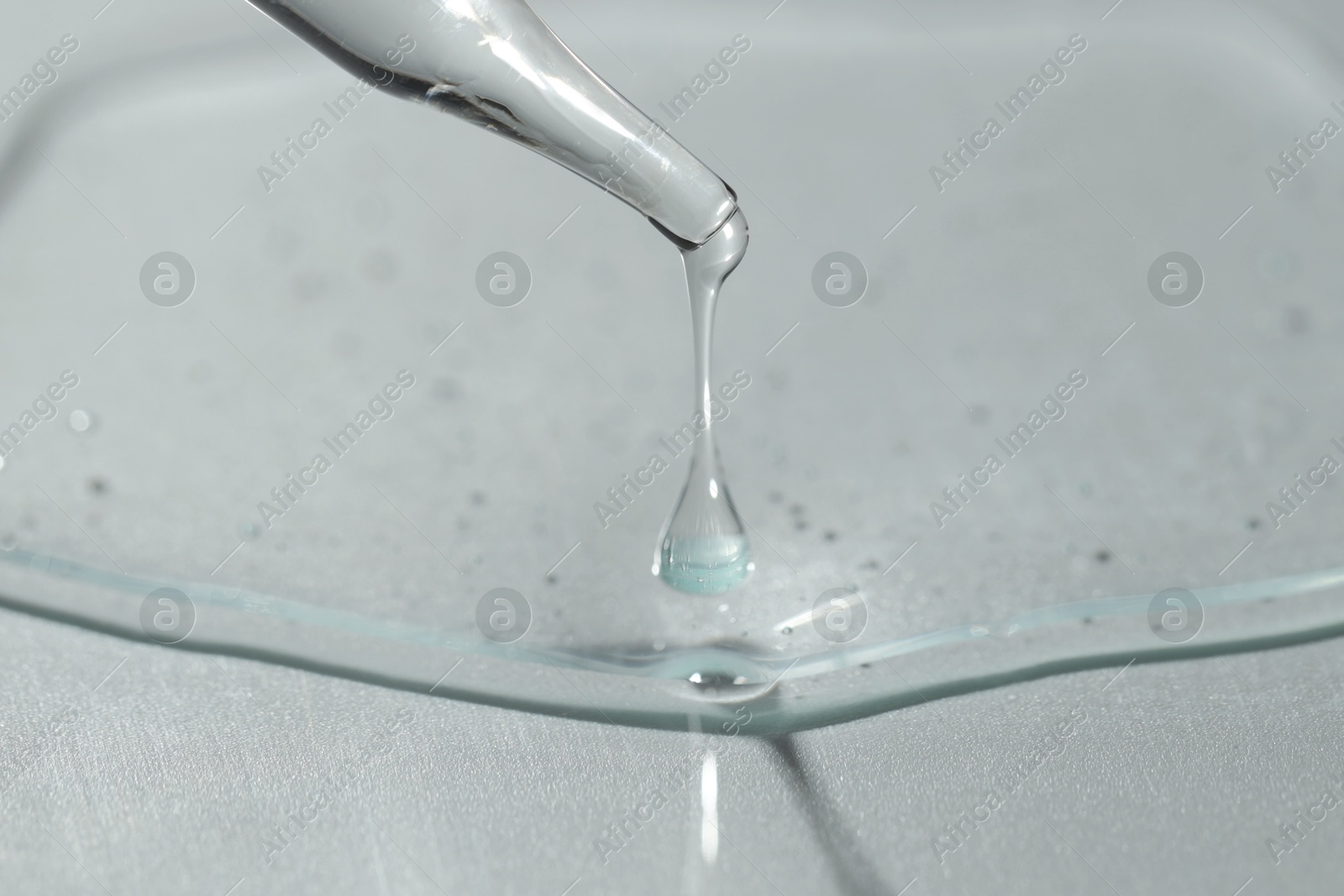 Photo of Dripping cosmetic serum from pipette on light background, closeup