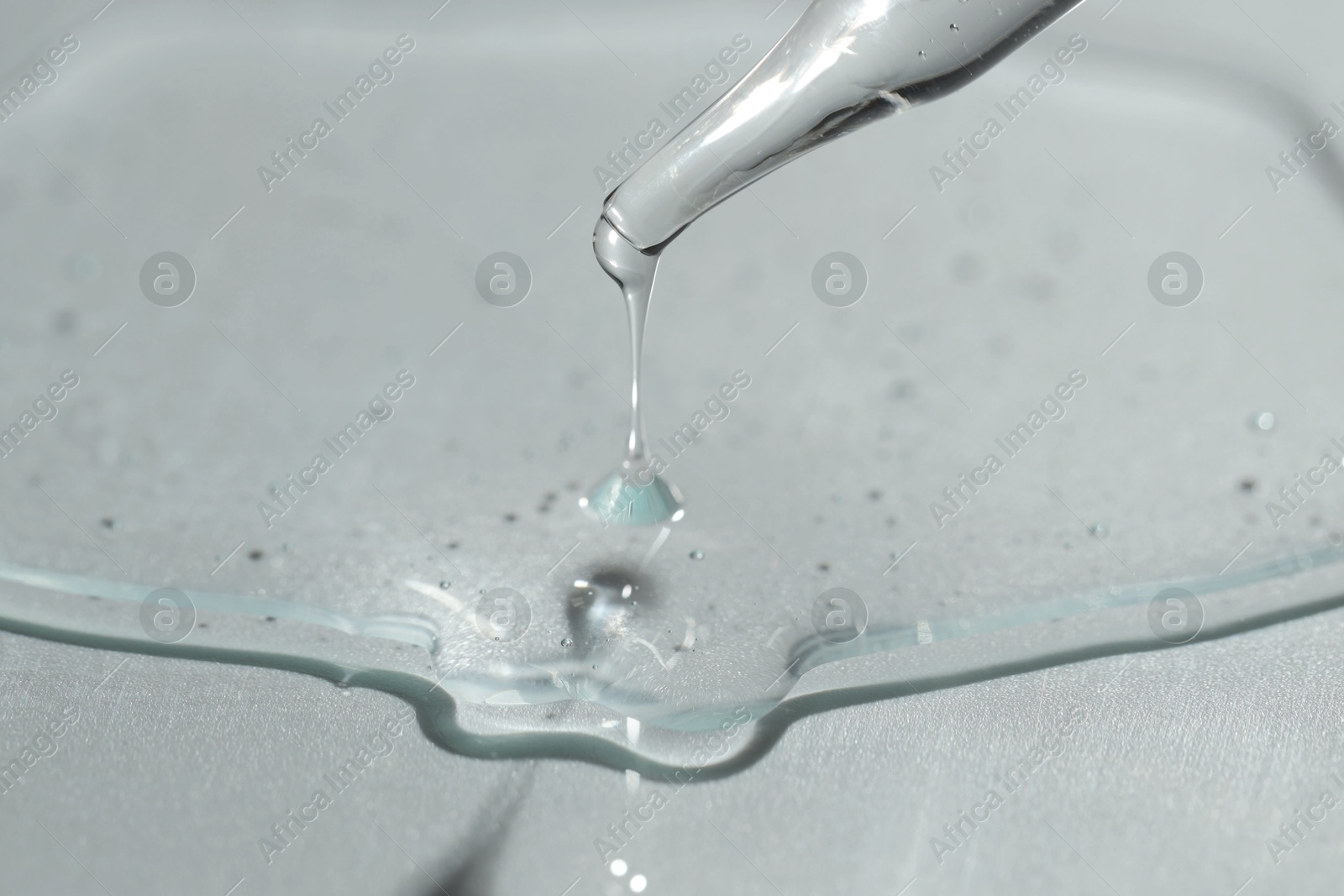 Photo of Dripping cosmetic serum from pipette on light background, closeup