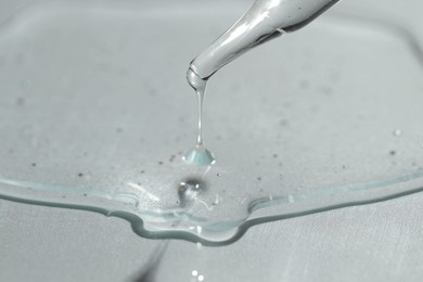 Photo of Dripping cosmetic serum from pipette on light background, closeup