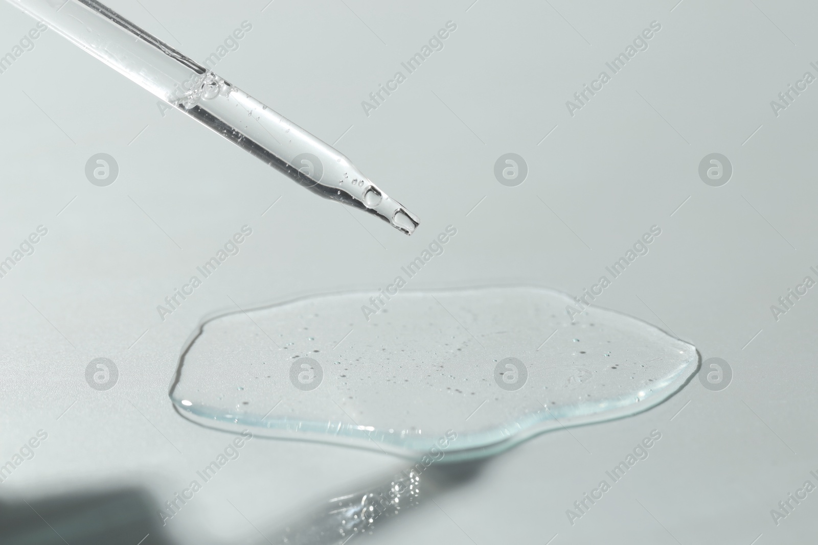 Photo of Dripping cosmetic serum from pipette on light background, closeup