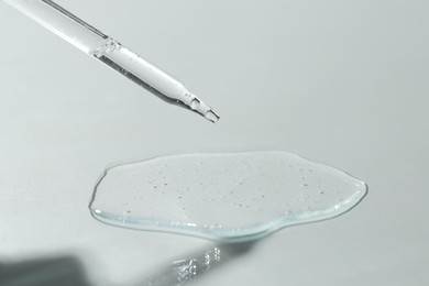 Dripping cosmetic serum from pipette on light background, closeup