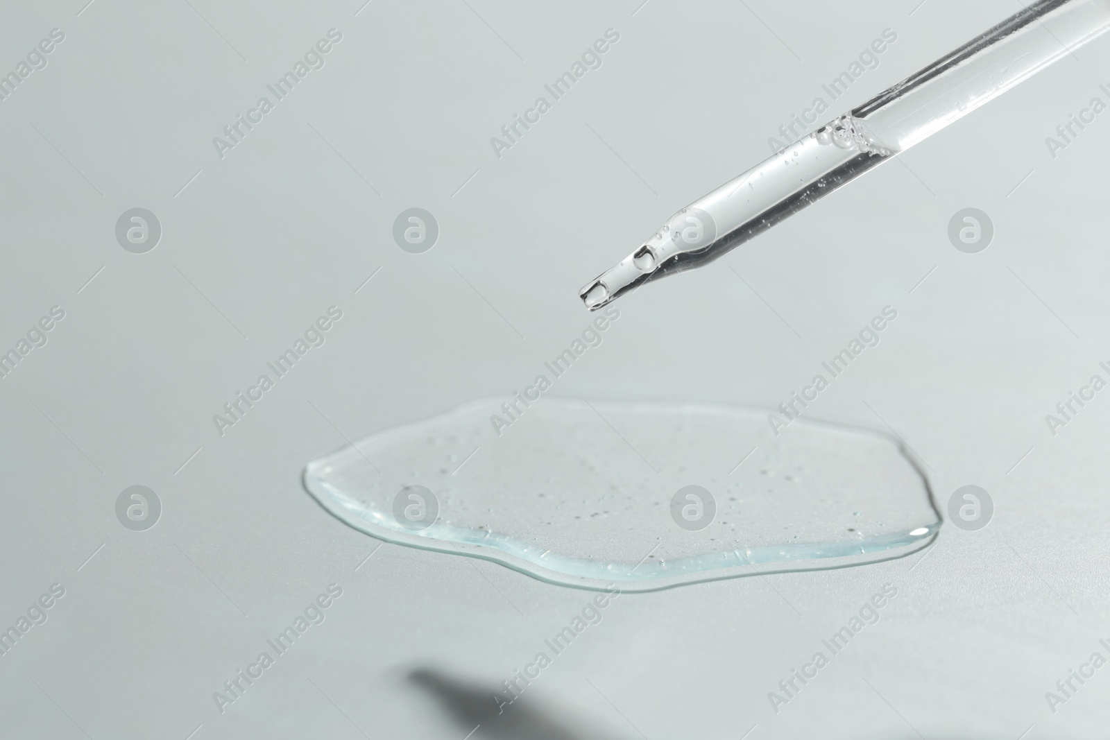 Photo of Dripping cosmetic serum from pipette on light background, closeup