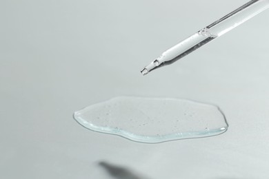 Photo of Dripping cosmetic serum from pipette on light background, closeup