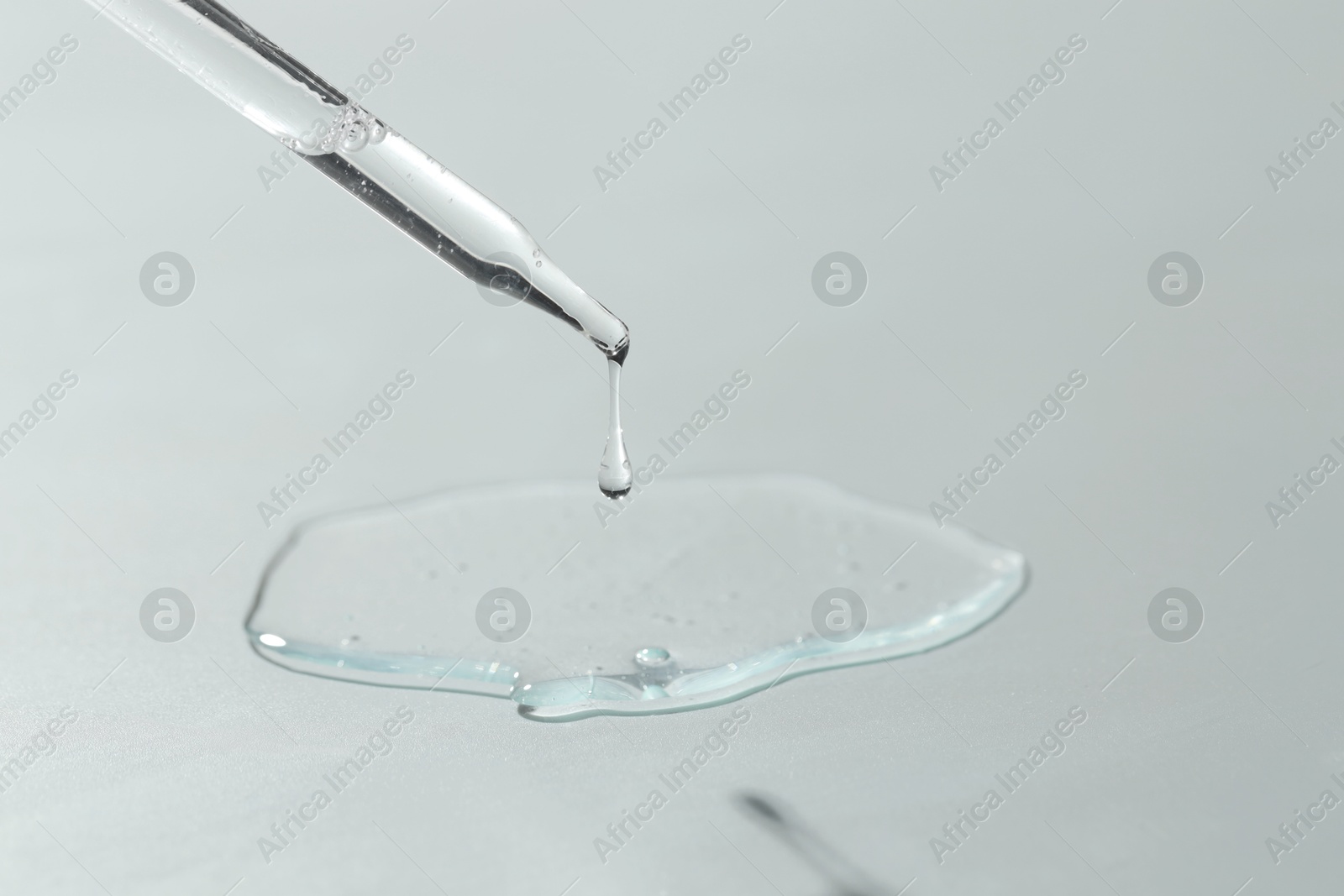 Photo of Dripping cosmetic serum from pipette on light background, closeup