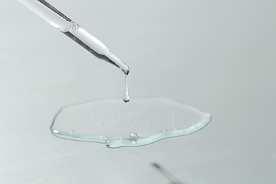 Photo of Dripping cosmetic serum from pipette on light background, closeup