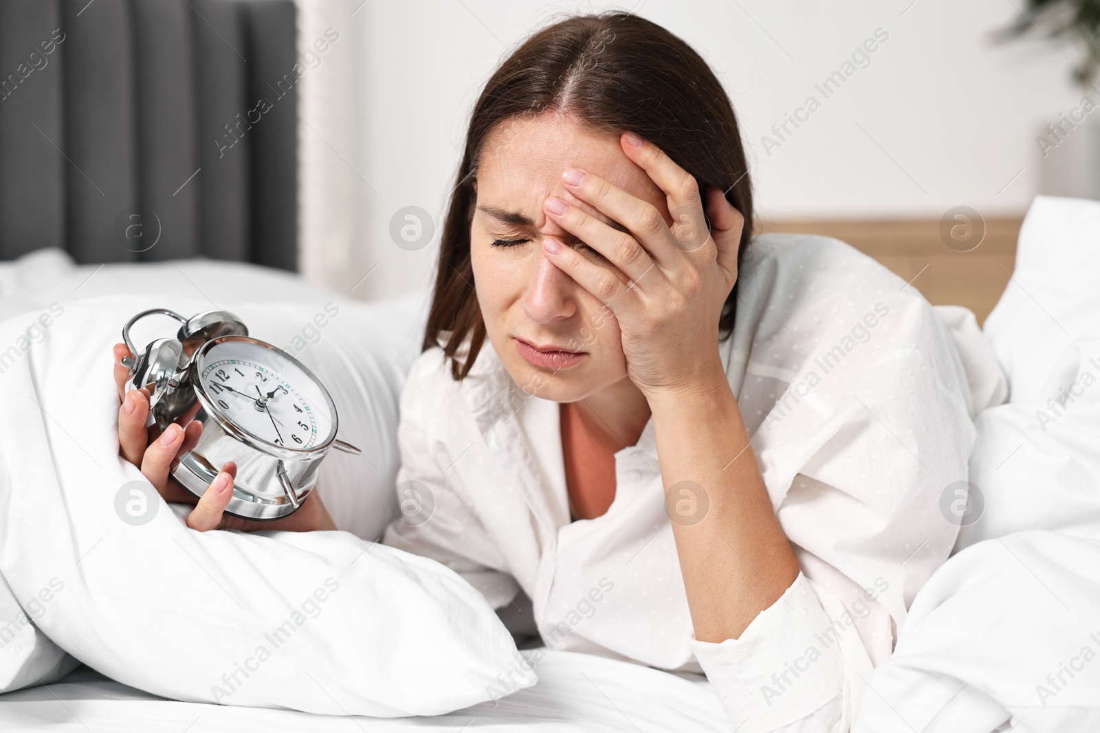 Photo of Sleepy woman waking up with alarm clock in bed at lunch time