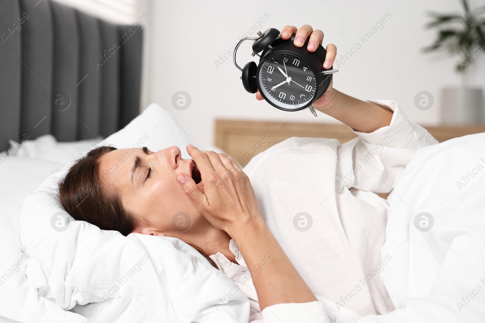 Photo of Sleepy woman with alarm clock in bed at lunch time