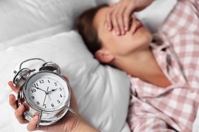 Woman waking up with alarm clock in bed at lunch time, selective focus