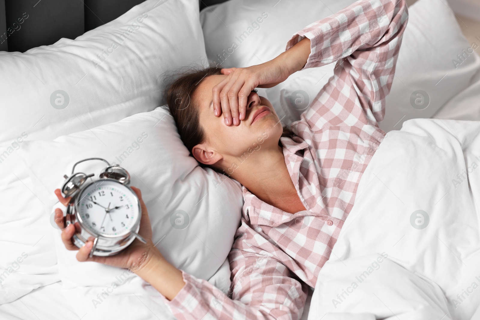 Photo of Sleepy woman waking up with alarm clock in bed at lunch time