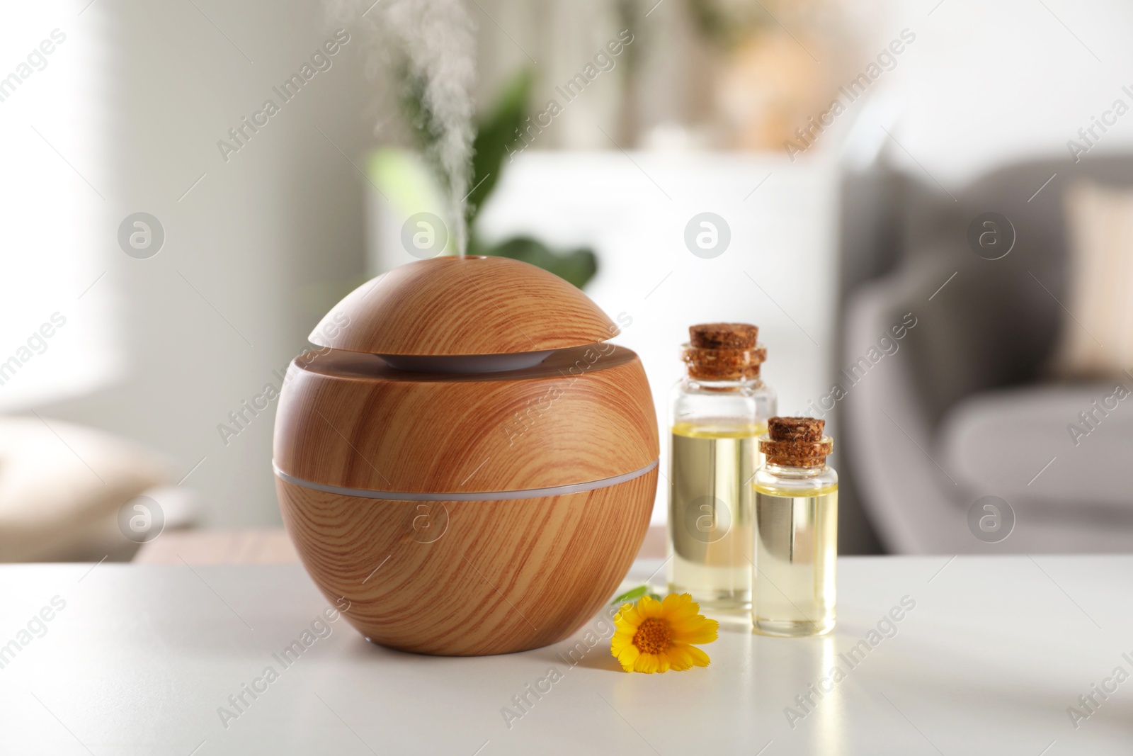 Photo of Essential oil diffuser, cosmetic products and calendula flower on white table at home