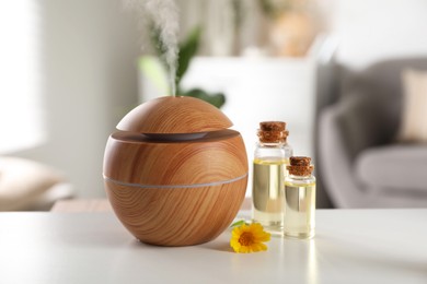 Essential oil diffuser, cosmetic products and calendula flower on white table at home