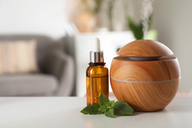 Photo of Essential oil diffuser, cosmetic product and mint on white table at home, space for text