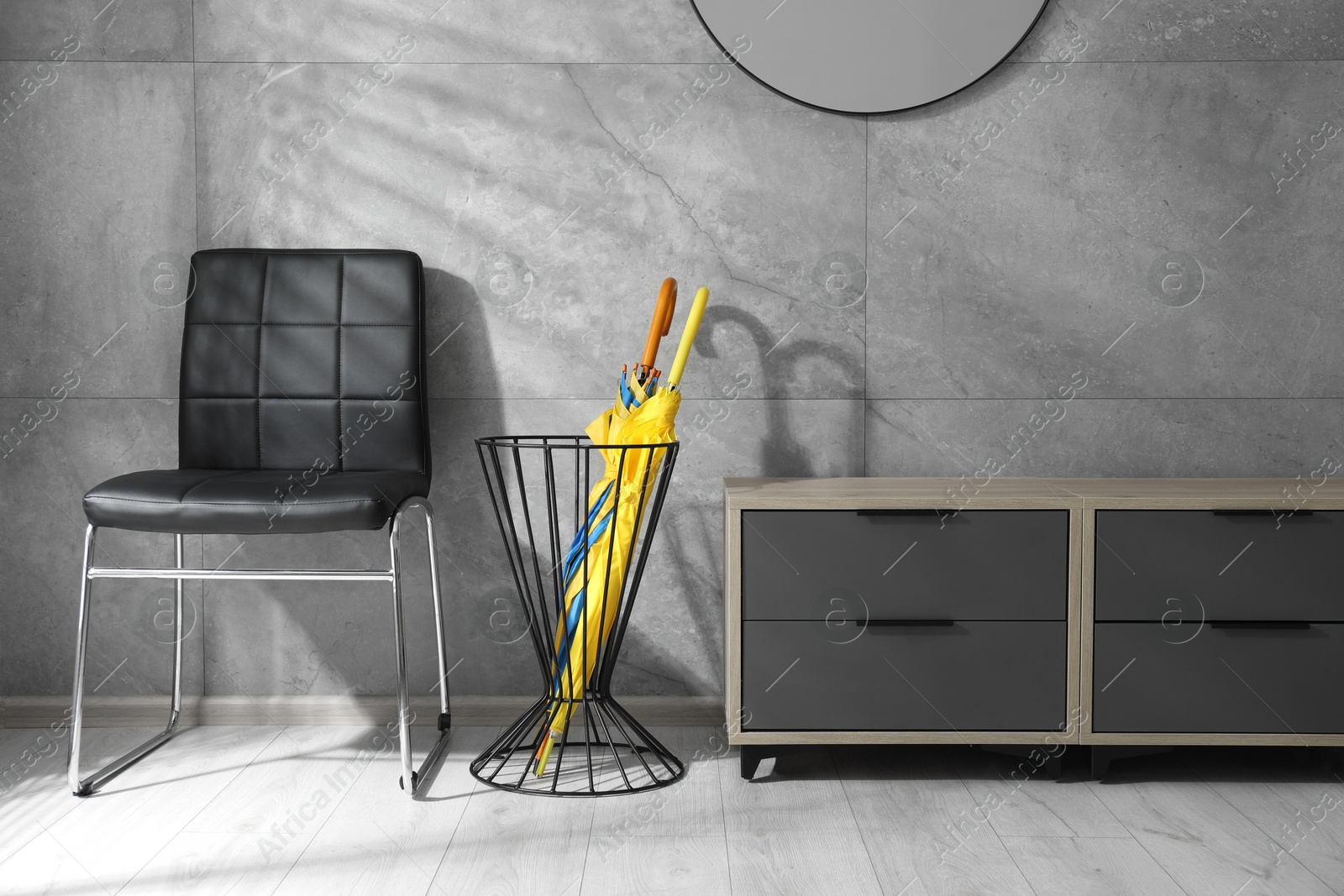 Photo of Holder with bright umbrellas, chair and cabinet on floor indoors