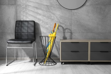 Photo of Holder with bright umbrellas, chair and cabinet on floor indoors