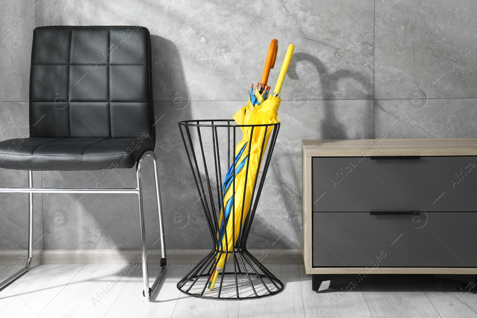 Photo of Holder with bright umbrellas, chair and cabinet on floor indoors