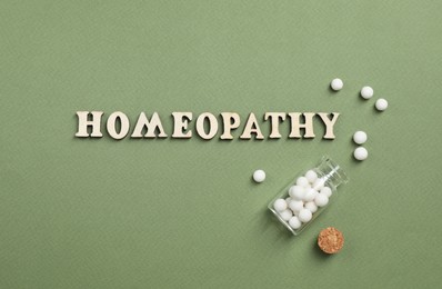 Photo of Word Homeopathy and pills on green background, flat lay