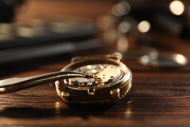 Mechanism of vintage wrist watch and tool on wooden table, closeup