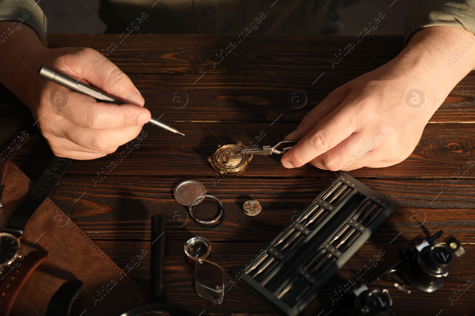 Photo of Man fixing mechanism of vintage wrist watch at wooden table, closeup