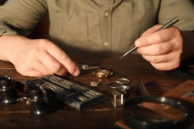 Photo of Man fixing mechanism of vintage wrist watch at wooden table, closeup