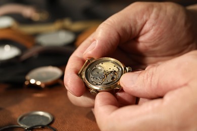 Photo of Man with mechanism of vintage wrist watch at table, closeup