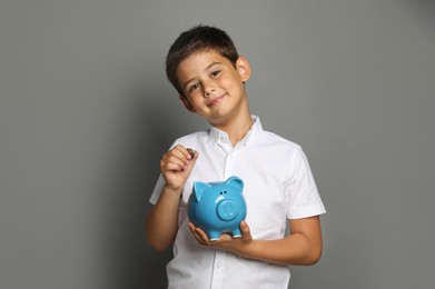 Photo of Pocket money. Cute boy with piggy bank and coins on grey background, space for text