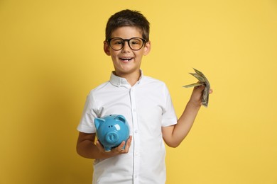 Photo of Cute boy with piggy bank and pocket money on yellow background