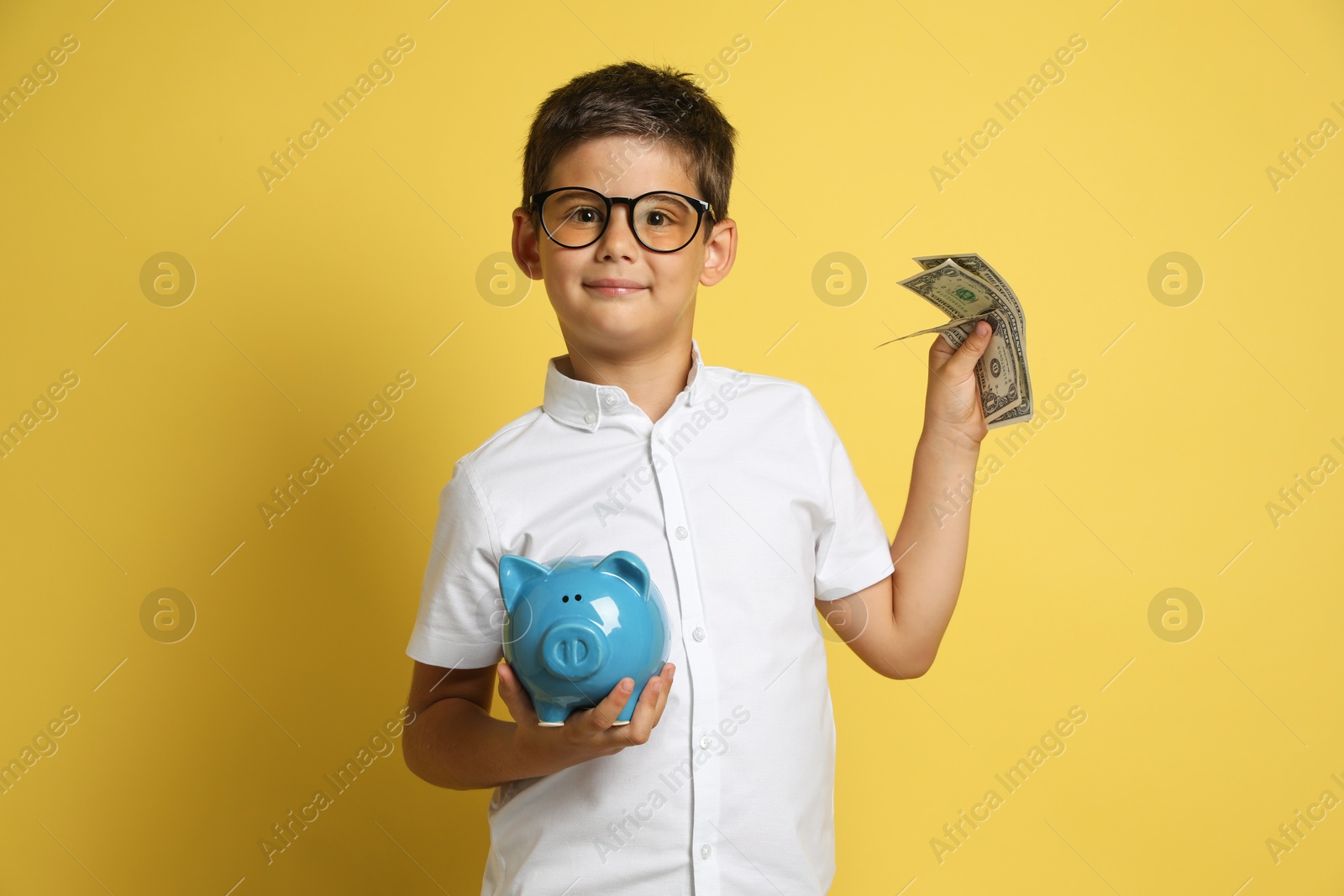 Photo of Cute boy with piggy bank and pocket money on yellow background