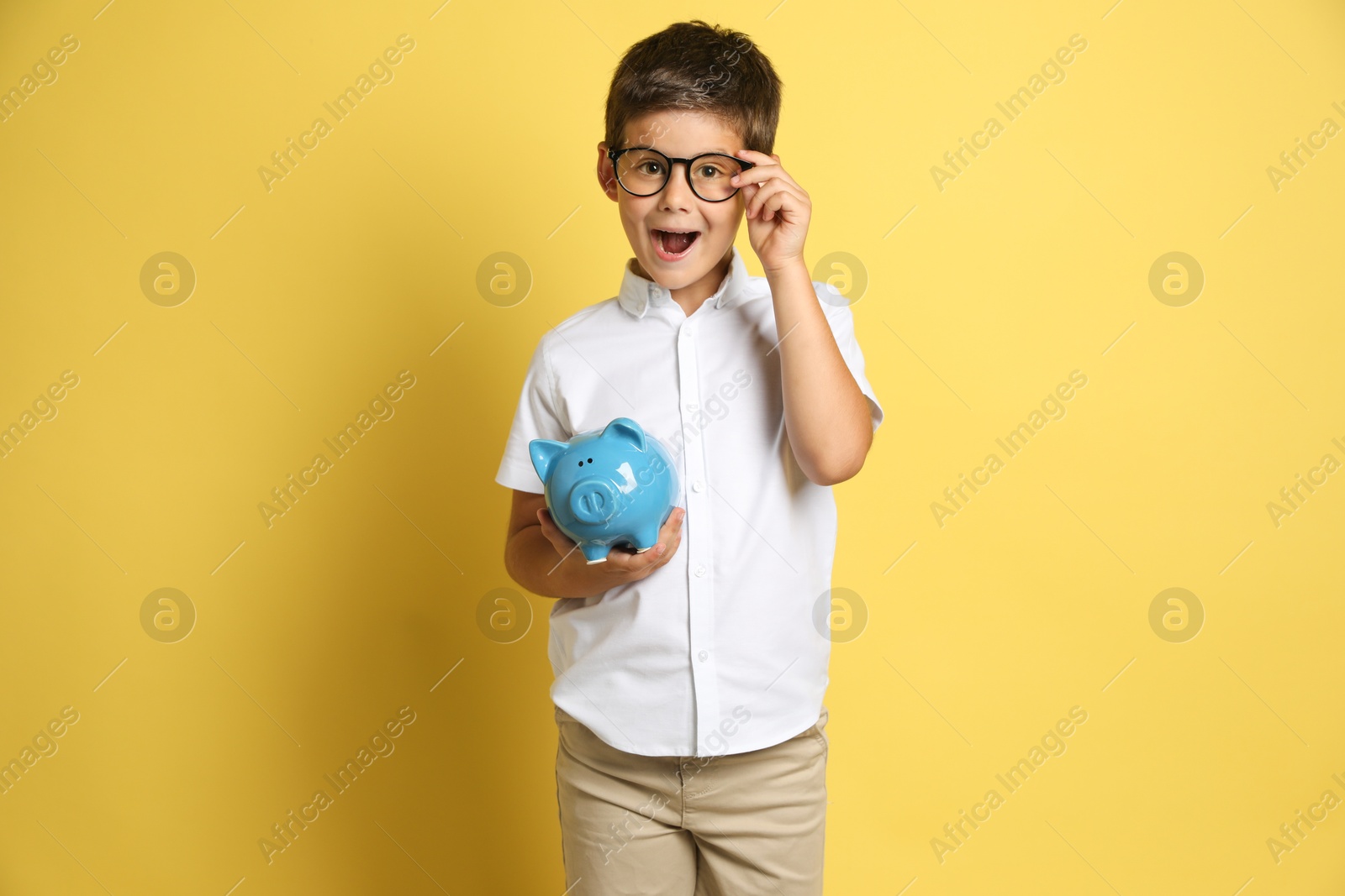 Photo of Pocket money. Cute boy with piggy bank on yellow background