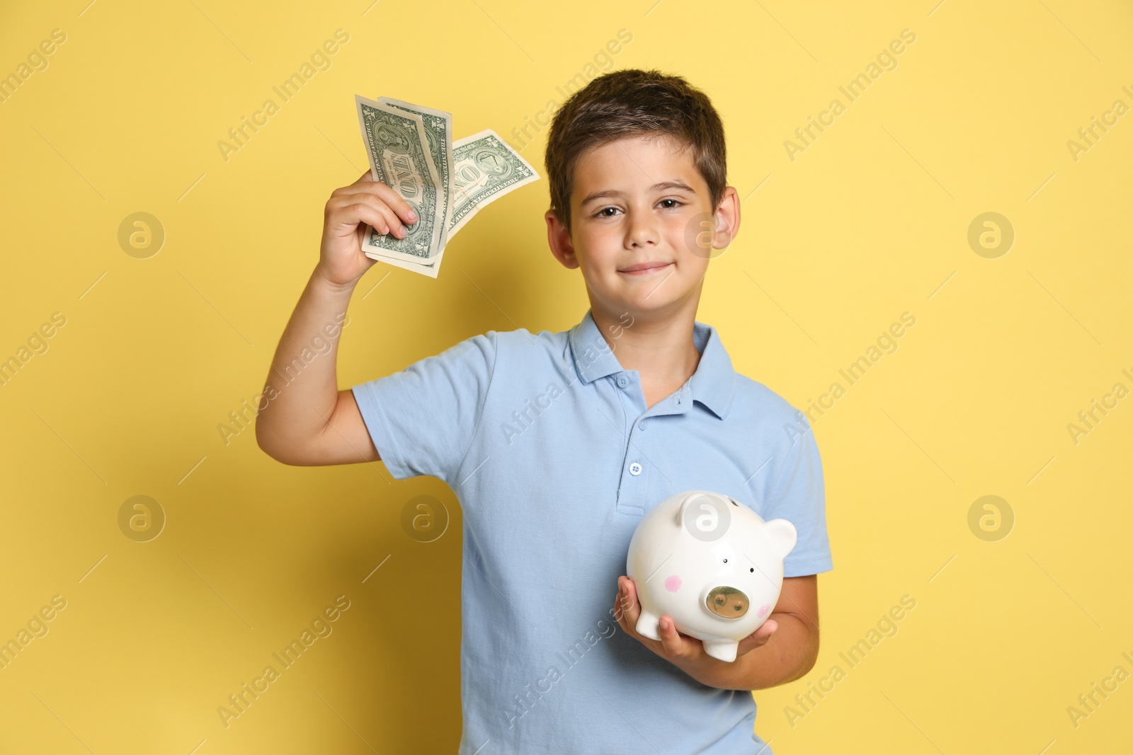 Photo of Cute boy with piggy bank and pocket money on yellow background