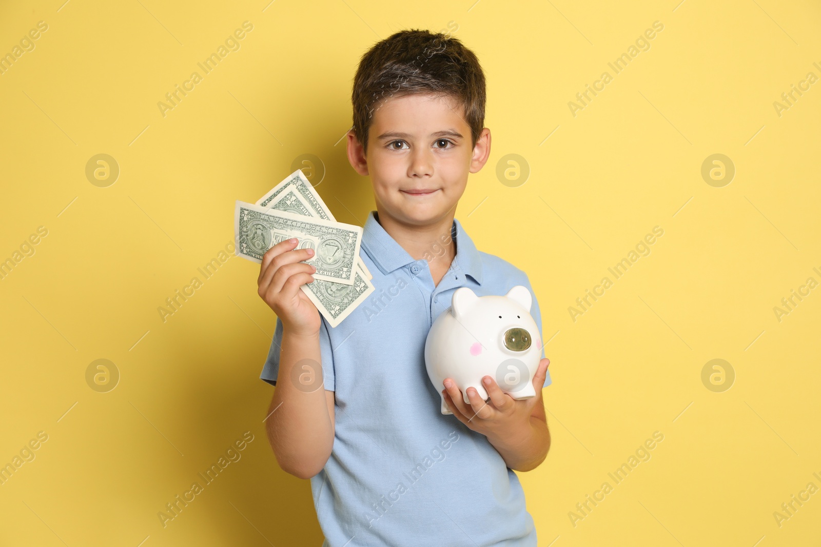 Photo of Cute boy with piggy bank and pocket money on yellow background