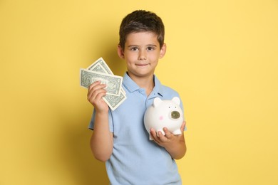 Photo of Cute boy with piggy bank and pocket money on yellow background