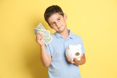 Cute boy with piggy bank and pocket money on yellow background