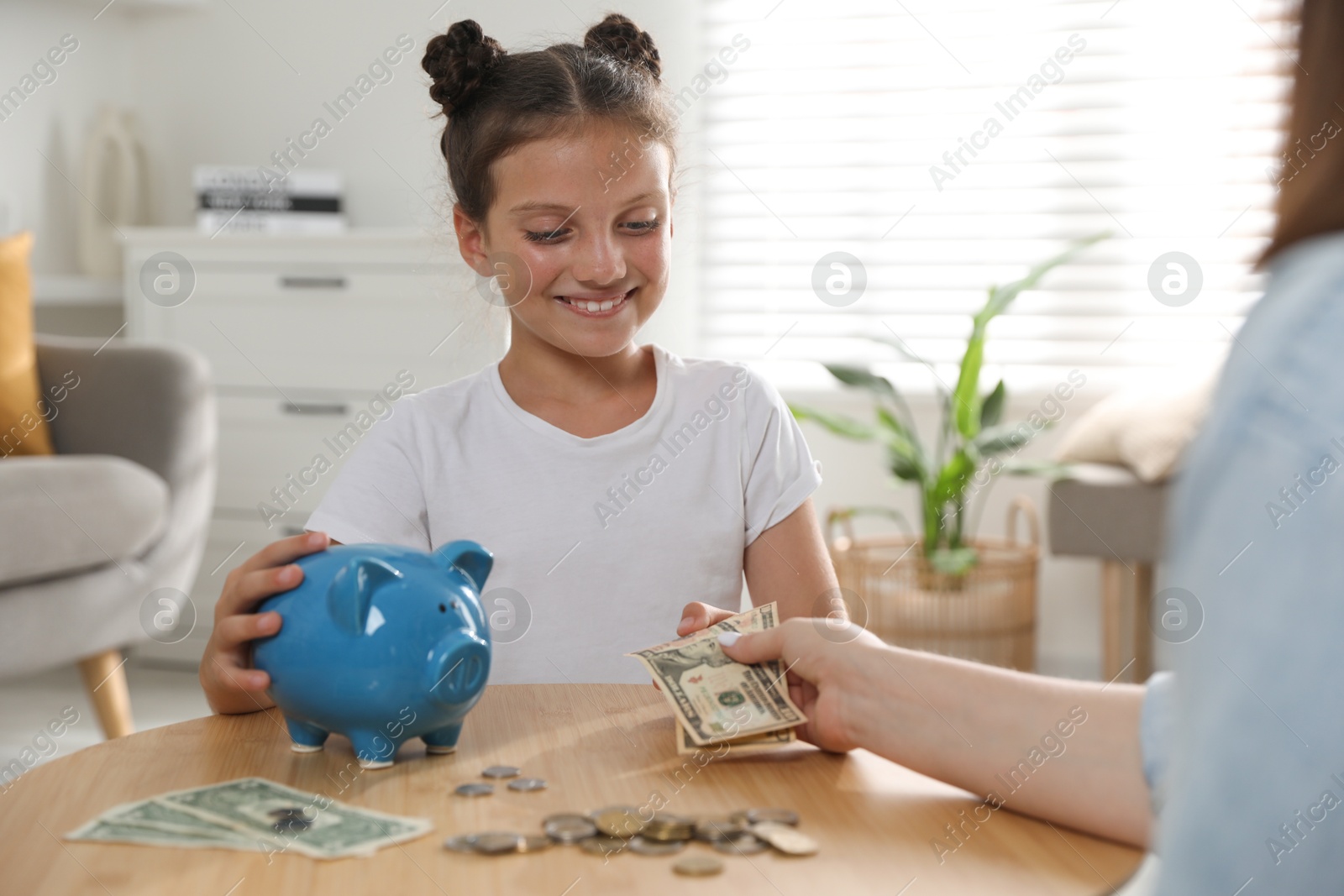 Photo of Mother giving pocket money to her daughter at table indoors