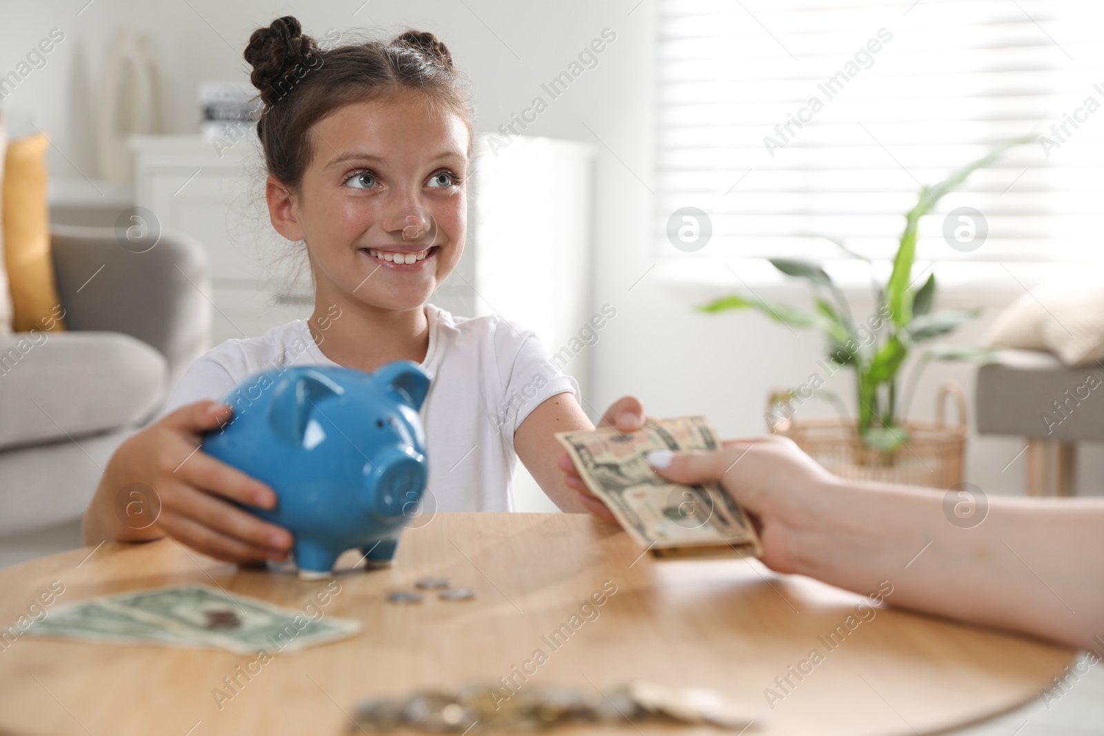 Photo of Mother giving pocket money to her daughter at table indoors