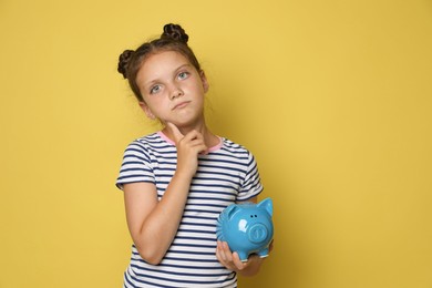 Photo of Pocket money. Cute girl with piggy bank on yellow background