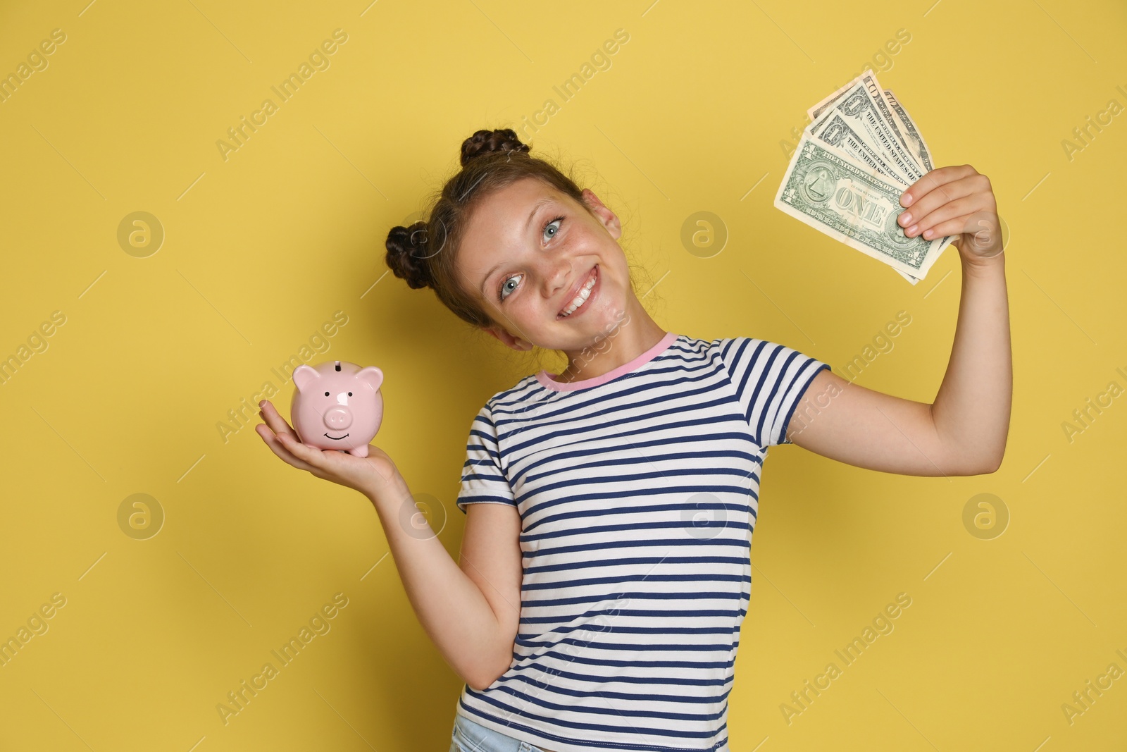 Photo of Pocket money. Cute girl with piggy bank and dollar banknotes on yellow background